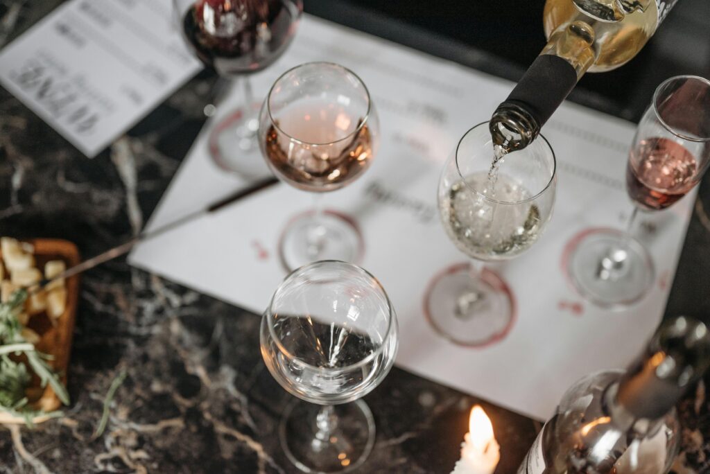Overhead view of a wine tasting setup on a marble table with white wine being poured and cheese platter nearby.